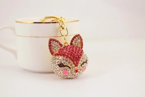 Close-up of red and white rhinestone fox keychain with gold metal clasp on a ceramic cup