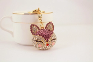Macro detail of fox keychain with purple crystals and gold metal finish on white backdrop