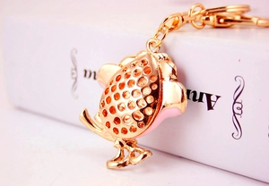 Close-up of a pink enamel fish-shaped keychain in gold metal on a clean white background