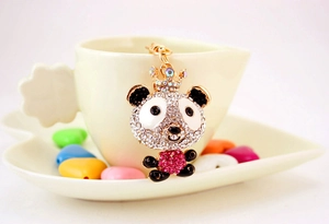 Detail shot of a cute crystal panda keychain with crown hanging on a cream coffee cup