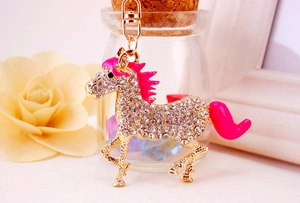 Close-up of golden horse keychain with white rhinestones and rose red mane on floral background