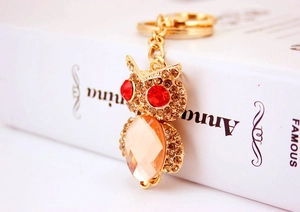 Close-up of golden owl keychain with red gemstone eyes and yellow crystals on book