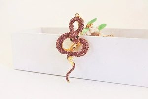 Détail d'un porte-clés serpent doré serti de strass violets sur une boîte blanche