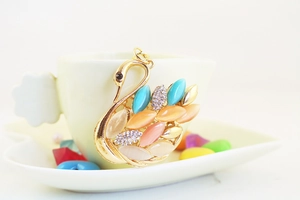 Detailed macro of crystal swan pendant with multi-color opal wings on ceramic cup