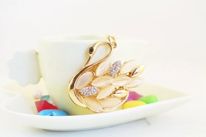 Detail shot of a gold swan keychain with marquise opals and rhinestones on a white cup