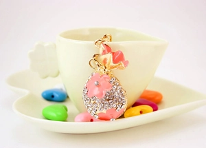 Détail d'un porte-clés sac de fortune doré avec strass et fleurs en émail rose sur tasse