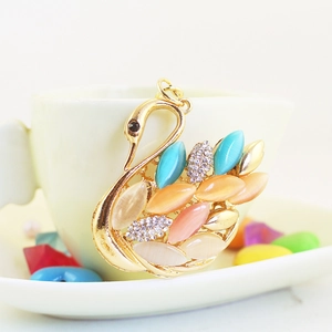 Elegant swan keychain with colorful opal stones and rhinestones on a white coffee cup