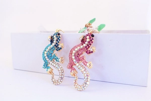 Vue détaillée de pendentifs lézard en strass colorés bleu et rose sur boîte cadeau