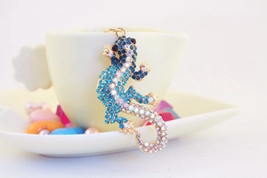 Porte-clés gecko doré avec strass bleus suspendu à une tasse blanche, vue détaillée