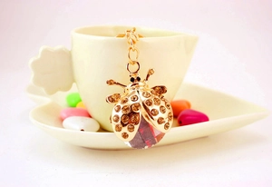 Détail du porte-clés coccinelle avec strass ambrés et cristal accroché à une tasse à café