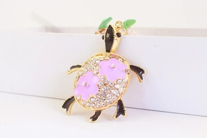 Détail macro du porte-clés tortue dorée avec strass brillants et fleurs en émail rose