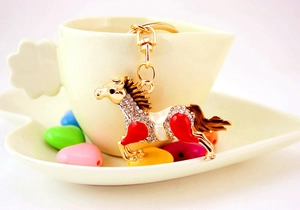 Detail of crystal horse keychain with golden metal finish and red enamel on a coffee cup