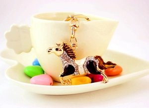 Macro detail of horse keychain with gold metal frame, white rhinestones and enamel finish
