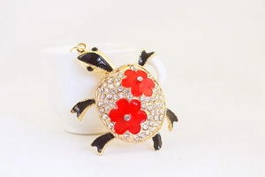 Vue détaillée du porte-clés tortue en strass avec fleurs en émail rouge et accents noirs