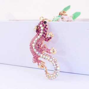 Porte-clés gecko en strass rose et doré suspendu sur une boîte cadeau avec fleurs