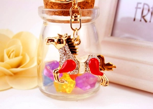 Detail view of gold horse keychain with white crystals and red enamel on decorative glass