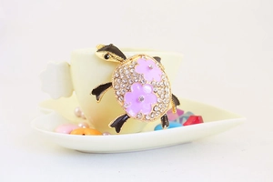 Détail d'un porte-clés tortue dorée avec strass blancs et petites fleurs mauves