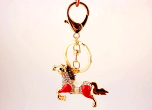 Detailed macro view of gold-plated horse keychain with clear crystals and red enamel finish