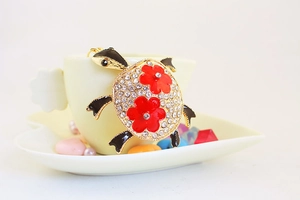 Détail du porte-clés tortue en cristal suspendu sur une tasse avec fleurs en émail rouge