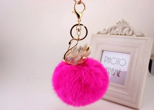 Dettaglio di un ciondolo a cigno dorato con strass e pompon di peluche color magenta