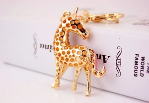 Detail of a golden giraffe keychain with cutout spots resting on a white book surface