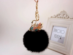 Dettaglio di un portachiavi a pompon nero con ciondolo a cigno dorato e cristalli colorati
