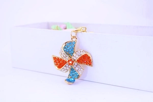 Close-up of a crystal windmill keychain featuring blue and orange rhinestones on a gold frame