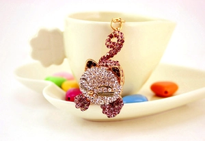 Détail d'un porte-clés chat doré avec strass blancs et violets sur une tasse en céramique