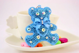 Detail of blue rhinestone teddy bear keychain with bow tie leaning against ceramic cup