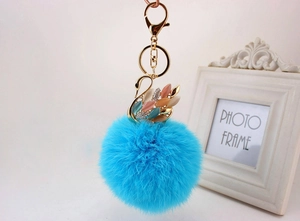 Dettaglio del pompon blu in ecopelliccia e portachiavi a cigno dorato con gemme