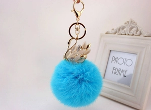 Dettaglio di un portachiavi a cigno dorato con pompon in pelliccia blu e strass lucidi