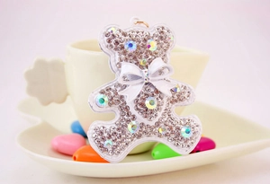 Detailed close-up of a white rhinestone bear keychain with a bow on a ceramic background