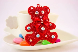 Detail of red rhinestone teddy bear pendant with a bow and AB crystals by a white cup