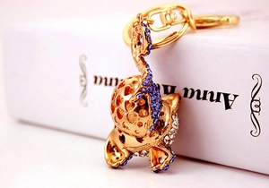 Détail d'un porte-clés chat doré serti de strass bleus et blancs avec découpes en cœur
