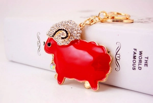 Detail of red enamel sheep keychain with rhinestones leaning against a white book