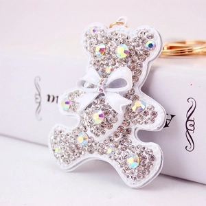 Sparkling white rhinestone bear keychain with bow and gold ring on a white book