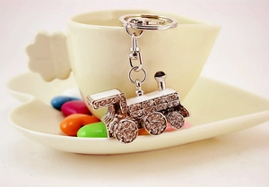 Detailed close-up of a vintage silver train keychain with rhinestones on a ceramic cup