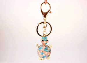 Detail of rhinestone turtle keychain with pink and blue opal stones on golden alloy base