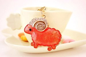 Close-up of golden goat keychain with orange enamel, rhinestones and spiral patterns
