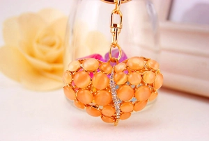 Detail van een gouden hartvormige sleutelhanger met oranje kattenoogstenen en strass