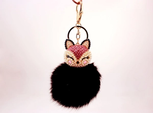 Detail of fox-shaped keychain with pink rhinestones, pearls, and black fluffy pom-pom