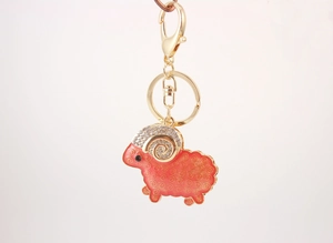 Close-up of golden sheep keychain with red enamel coating and crystal details