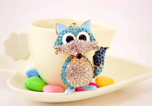 Close-up of blue crystal fox keychain with gold metal frame hanging on a white ceramic cup