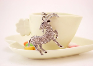 Dettaglio macro del portachiavi a forma di capra argentata con strass lucidi su una tazza