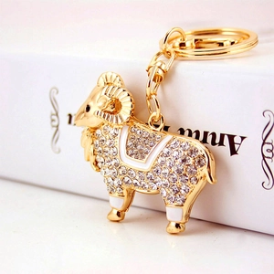 Porte-clés chèvre dorée avec strass et détails en émail blanc sur un support élégant