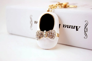 Close-up of a white enamel mini shoe keychain with a rhinestone bow and gold details