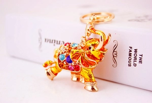 Detail of a golden elephant keychain with colorful rhinestones on a white book edge