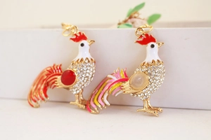 Macro detail of rooster keychain charms with crystals, enamel work, and red gemstones
