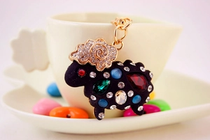 Détail d'un porte-clés mouton noir avec strass colorés accroché à une tasse en céramique