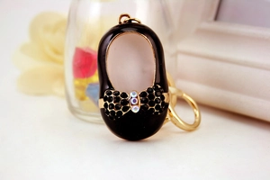 Detail of a black ballet shoe keychain with a rhinestone bow and golden metal accents